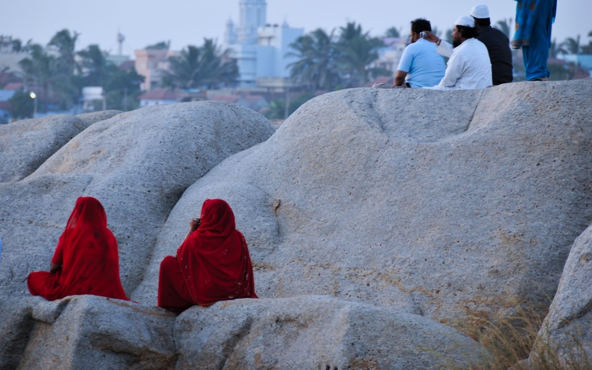 two women in red sari perched on the rock looking out into the horizon