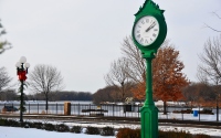 a green clock by the side of the road : a clock and street lamp a road and a river