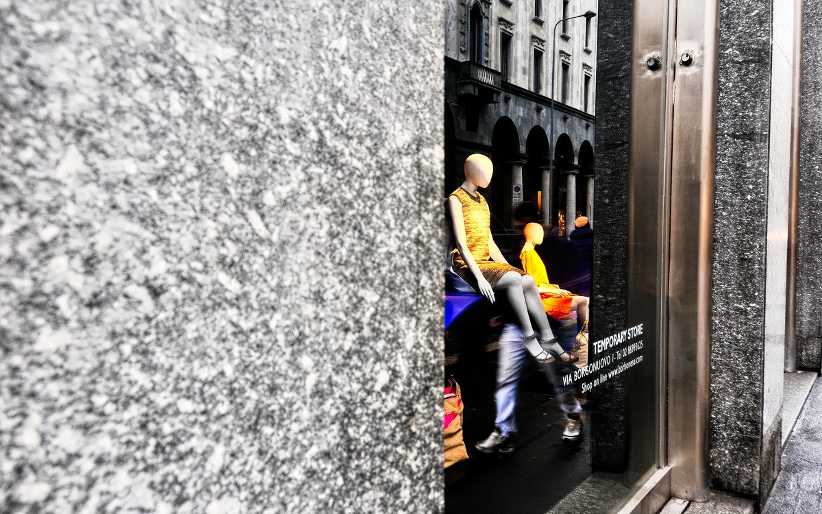 a storefront with mannequins and reflections of the buildings